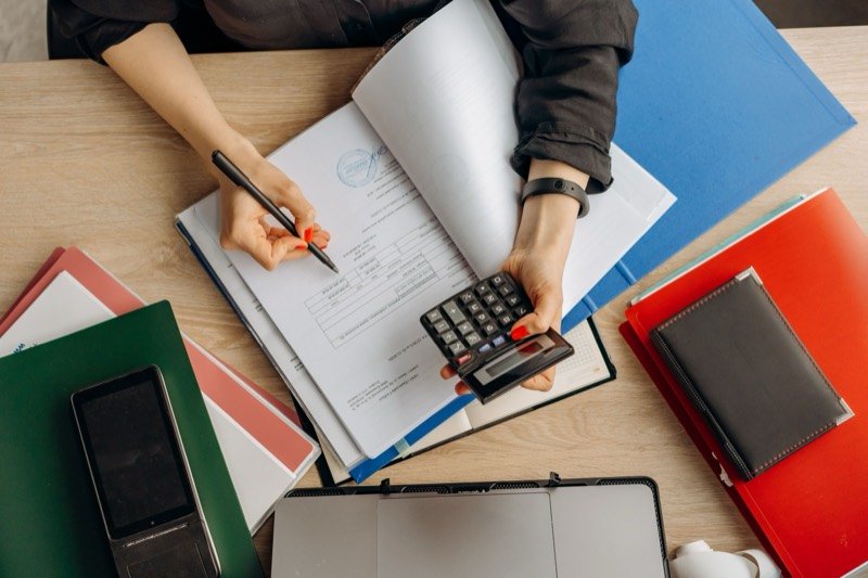 Hands working through paper files with a calculator on a crowded desk